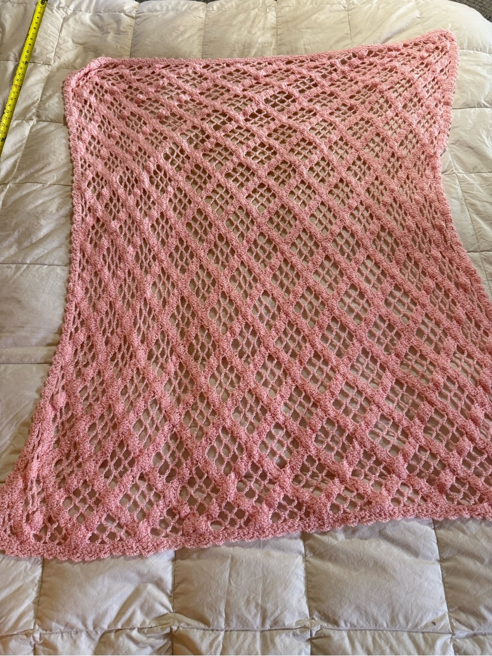 A light pink, handmade crochet blanket featuring an open-work diagonal or diamon